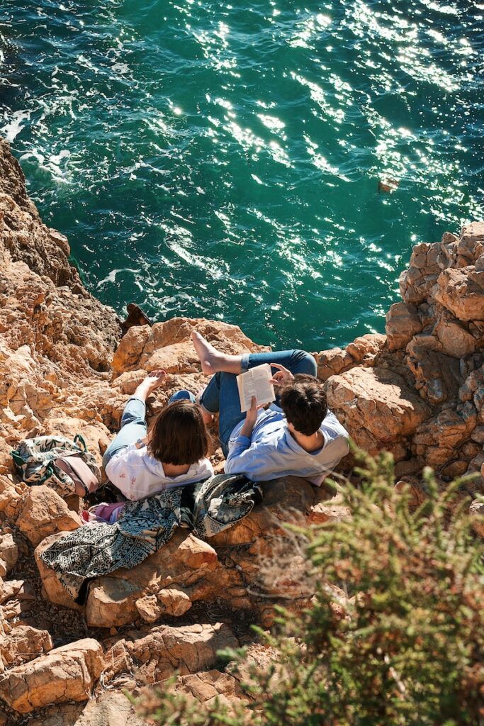 a couple of people sitting on some rocks by the water